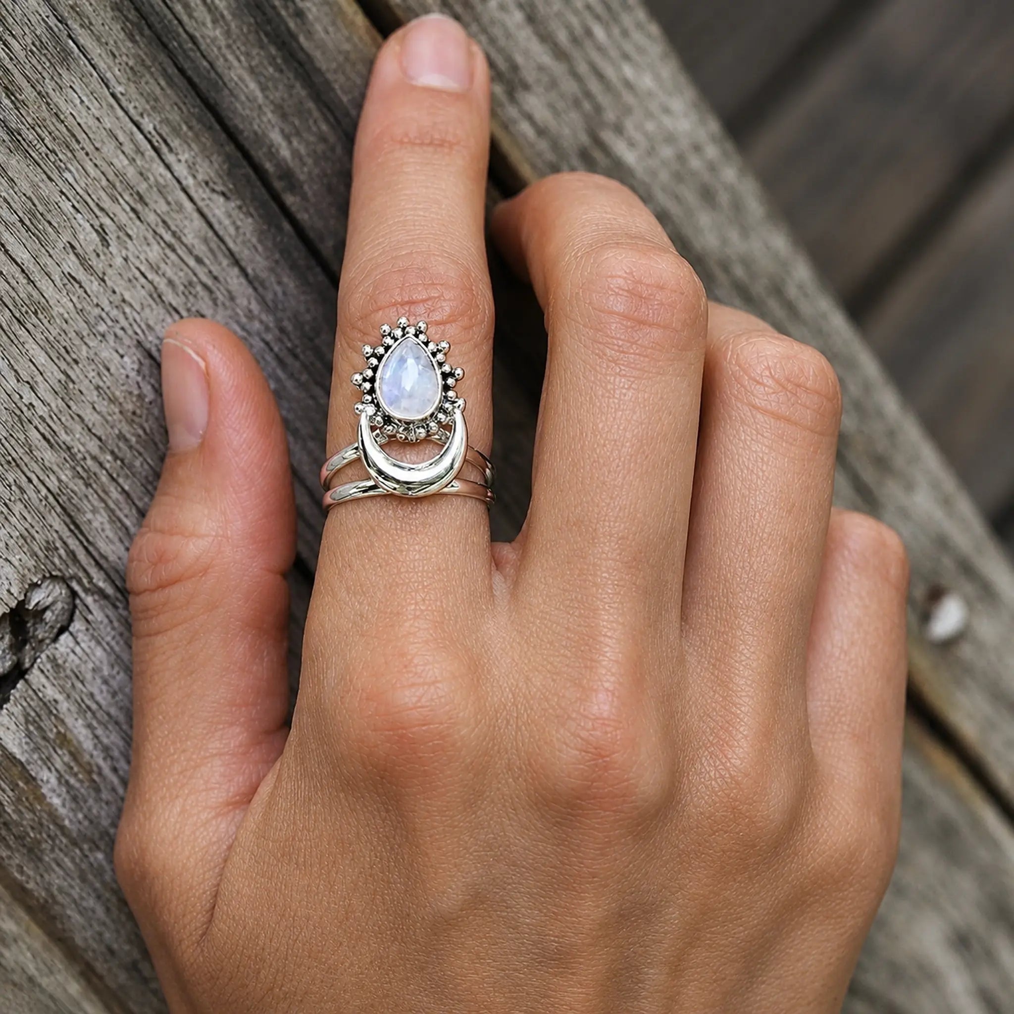 Hand wearing a rainbow moonstone crescent ring in polished sterling silver against rustic timber