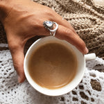 Hand wearing a rainbow moonstone crescent ring in sterling silver while holding a cup of coffee
