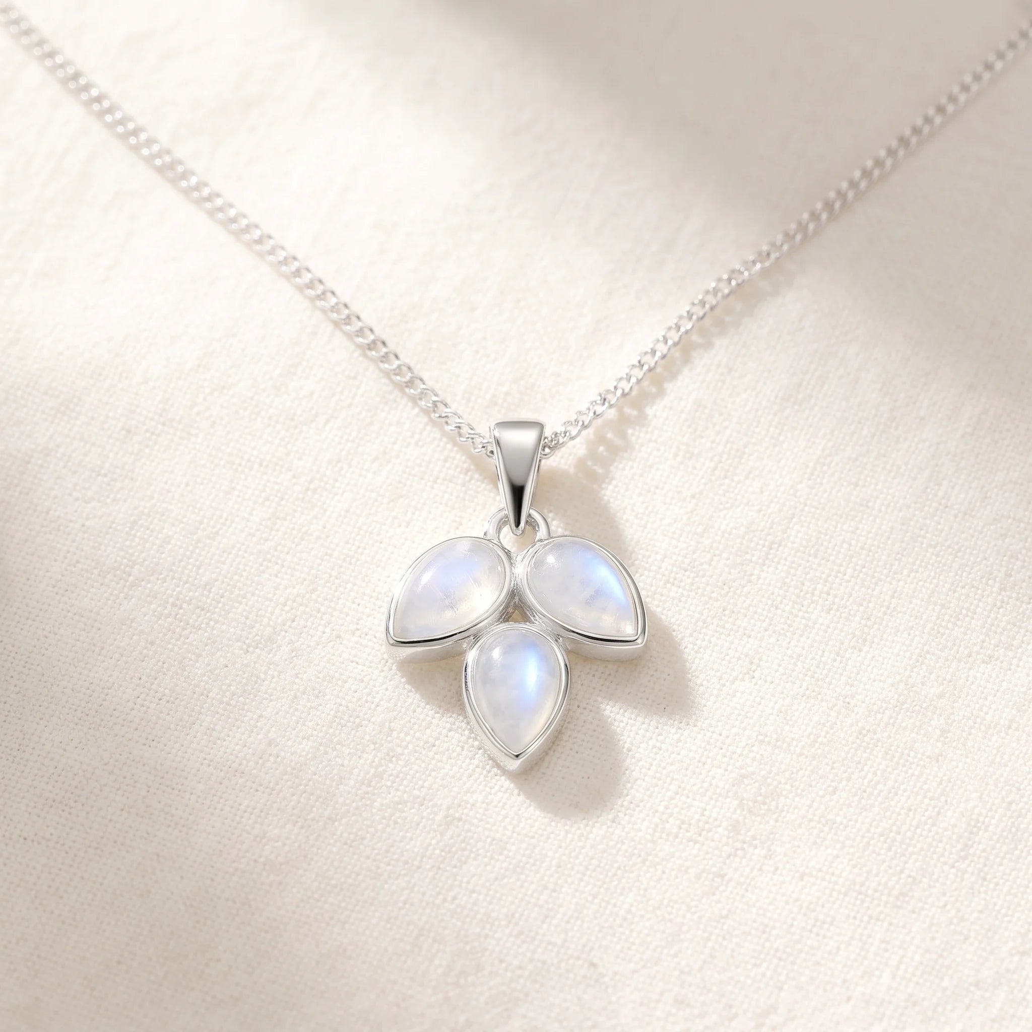 Rainbow moonstone leaf necklace flat lay on warm white linen, three pear-shaped moonstones on a fine silver curb chain