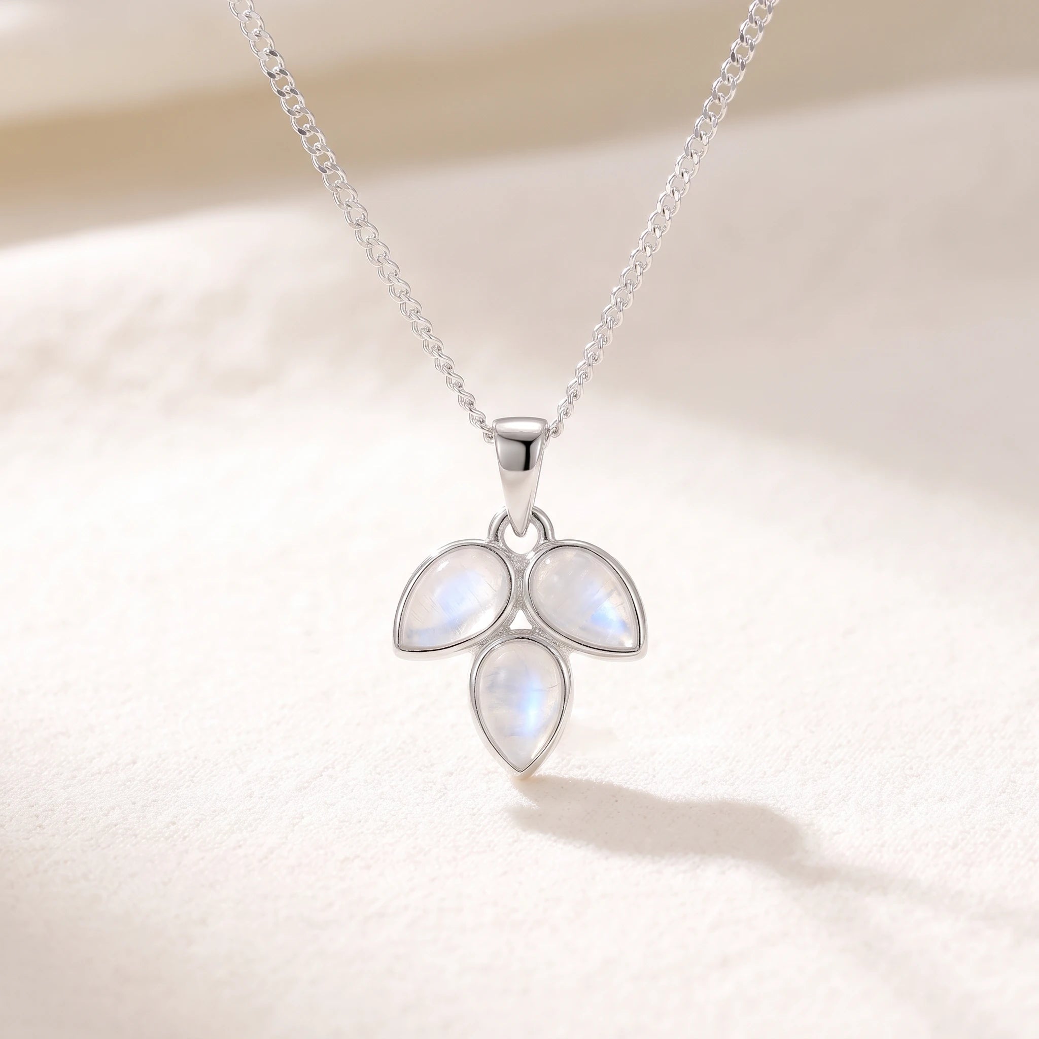 Rainbow moonstone leaf necklace hanging against a soft warm white background on a fine silver curb chain