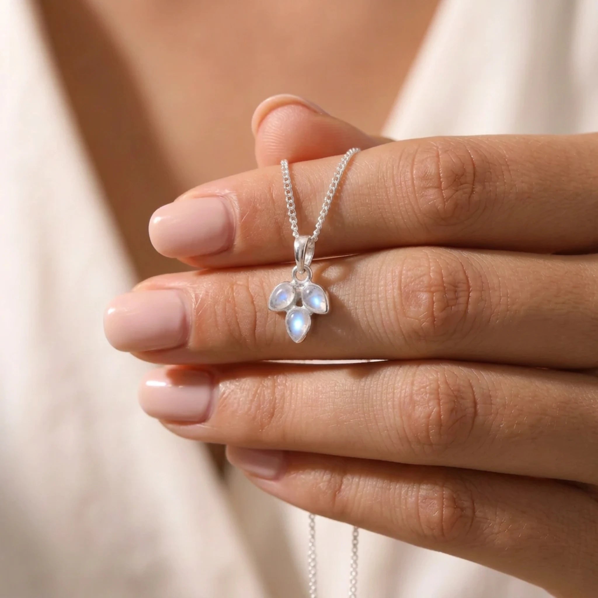 Rainbow moonstone leaf necklace held in fingers, three pear-shaped moonstones on a fine silver curb chain