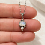 Rainbow moonstone and pearl necklace held between fingers showing dainty oxidised sterling silver pendant scale