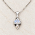 Rainbow moonstone and pearl necklace close-up on cream marble, oval moonstone above a small freshwater pearl