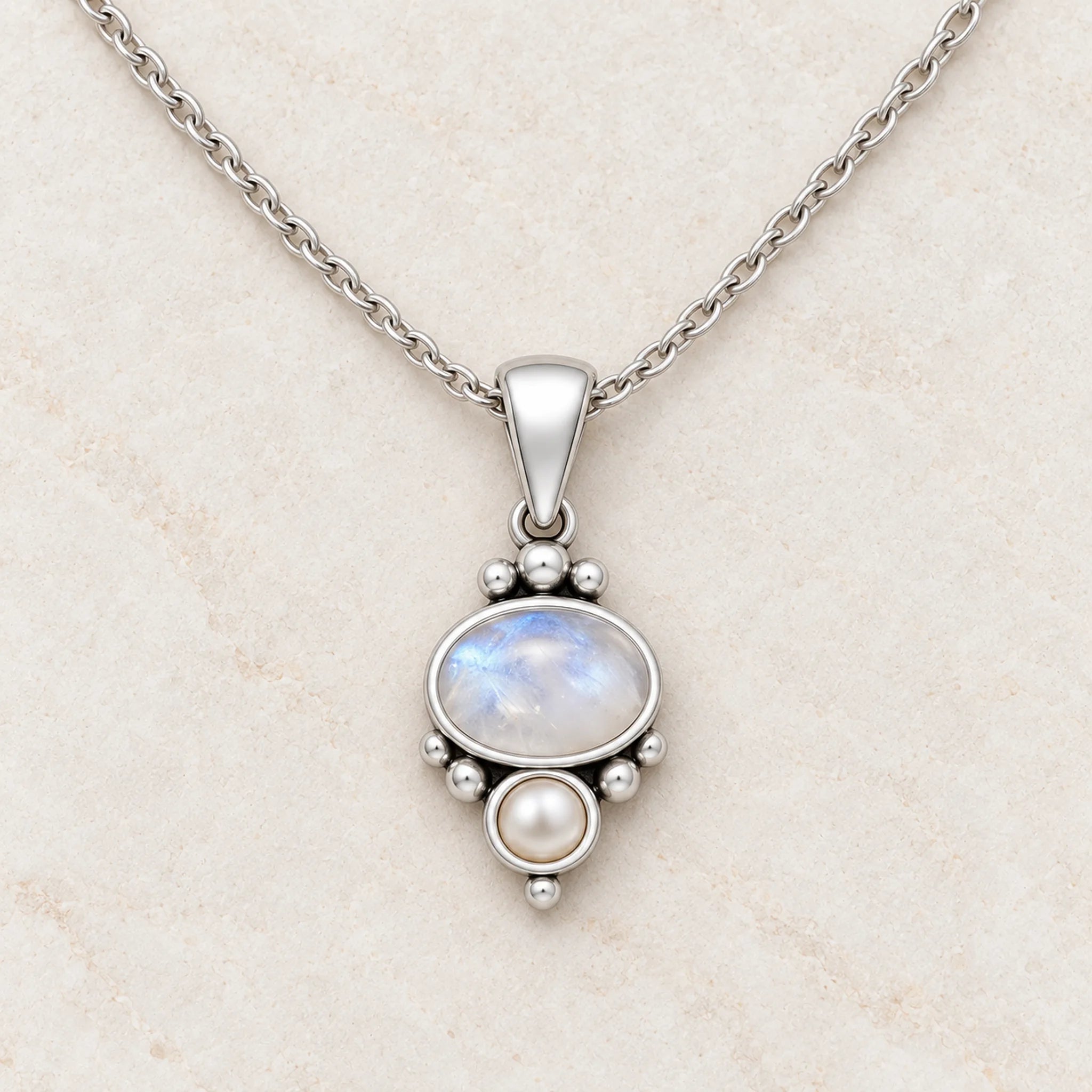 Rainbow moonstone and pearl necklace close-up on cream marble, oval moonstone above a small freshwater pearl