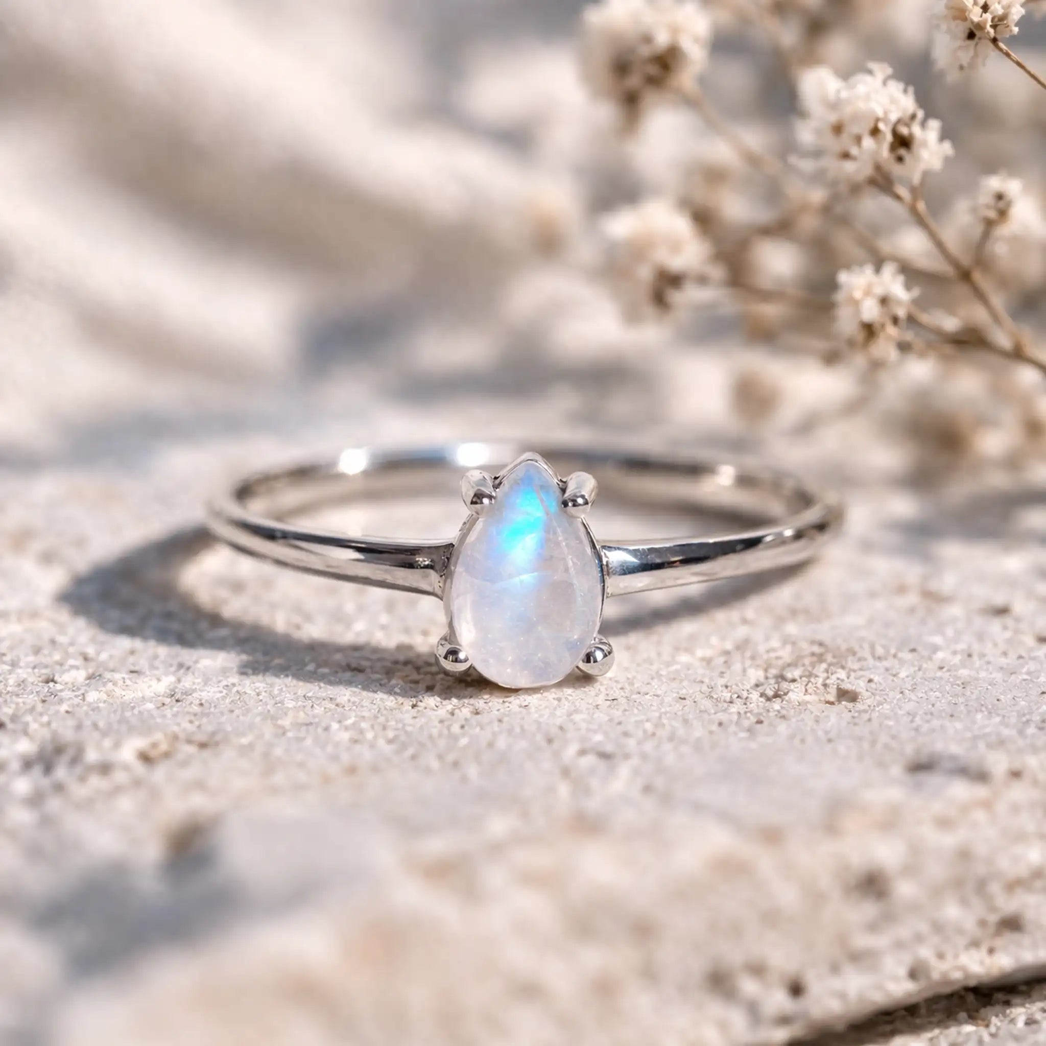Close-up of a dainty 925 sterling silver ring with a pear-shaped rainbow moonstone in a four-claw setting and blue flash