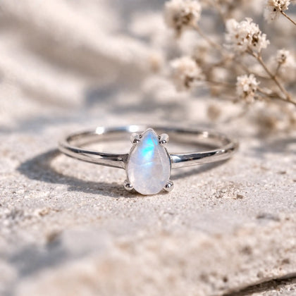 Close-up of a dainty 925 sterling silver ring with a pear-shaped rainbow moonstone in a four-claw setting and blue flash