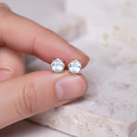 Silver stud earrings with natural rainbow moonstone gemstones held between fingers on a neutral background