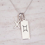 Sterling silver X initial and GeminI Necklace on a fine silver chain on a light wooden background