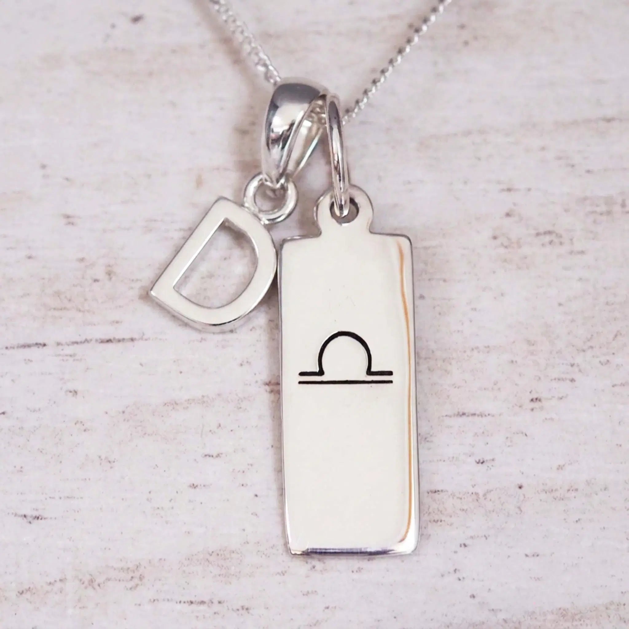 sterling silver initial d libra zodiac star sign pendant necklace against a light wooden background