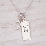 Sterling silver O initial and GeminI Necklace on a fine silver chain on a light wooden background