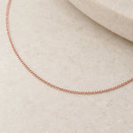 Soft 9k rose gold fine 1 mm curb chain close-up on ivory stone