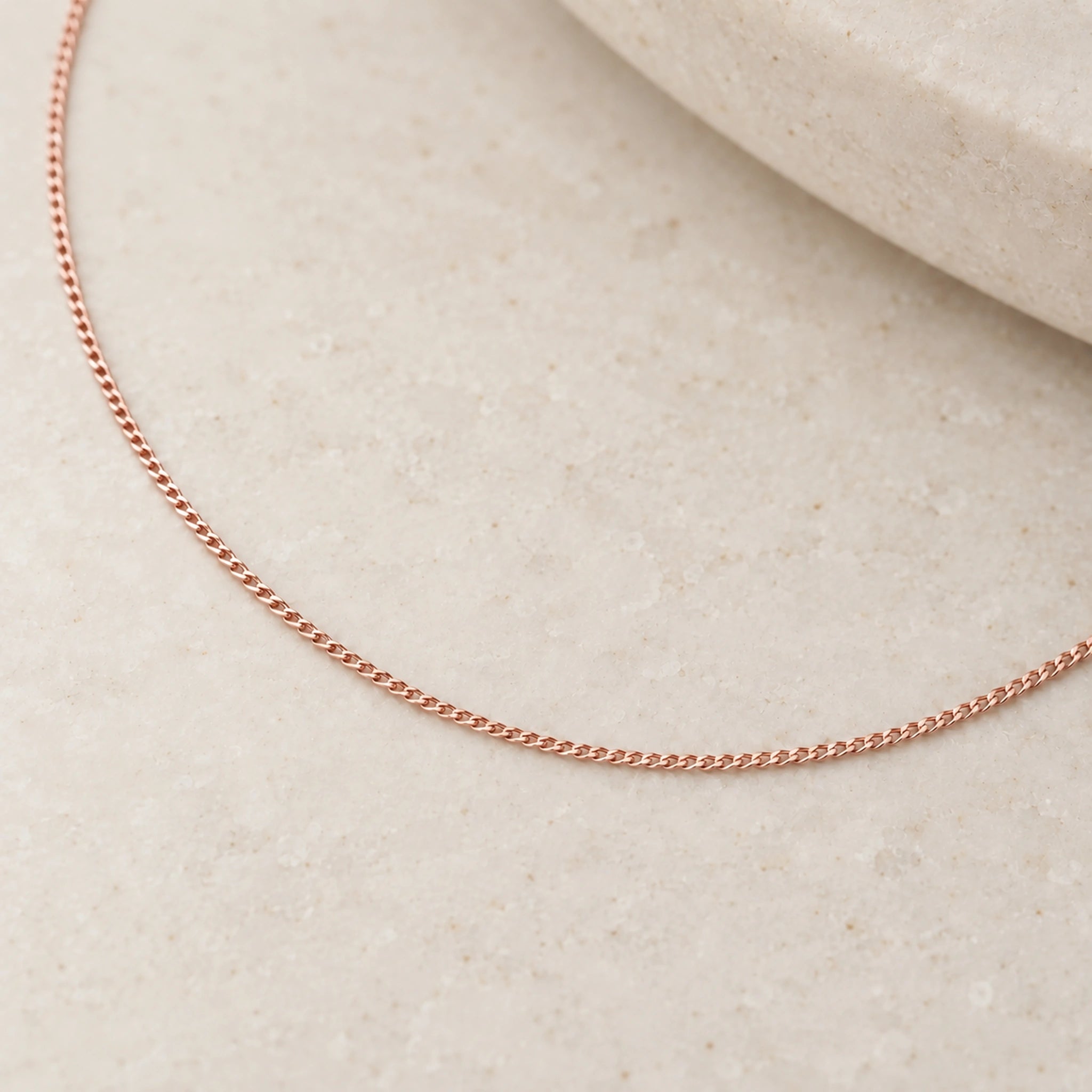 Soft 9k rose gold fine 1 mm curb chain close-up on ivory stone