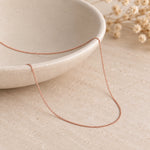 Fine 1 mm rose gold curb chain draped over an ivory ceramic bowl