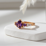 Rose gold ring with purple gemstone on a white surface with decorative elements