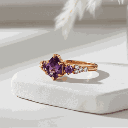 Rose gold ring with purple gemstone on a white surface with decorative elements