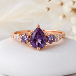 Rose gold ring with purple gemstone on a white stone with dried flowers in the background