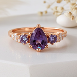 Rose gold ring with purple gemstone on a white surface with dried flowers.