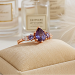 Ring with purple gemstone on a beige cushion in front of perfume bottles
