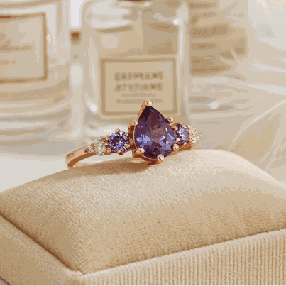 Ring with purple gemstone on a beige cushion in front of perfume bottles