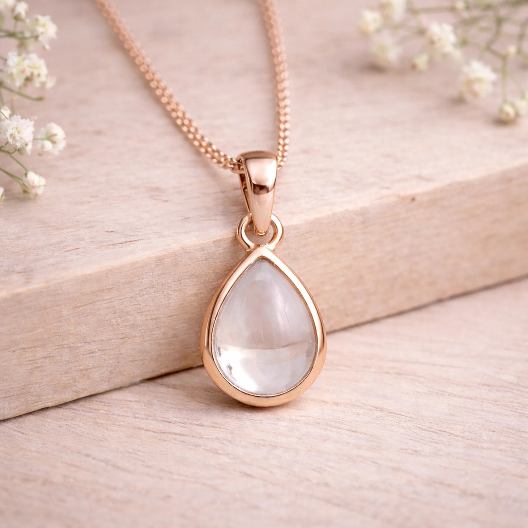 Rose Gold necklace with a teardrop-shaped natural herkimer quartz cabochon pendant on a wooden surface
