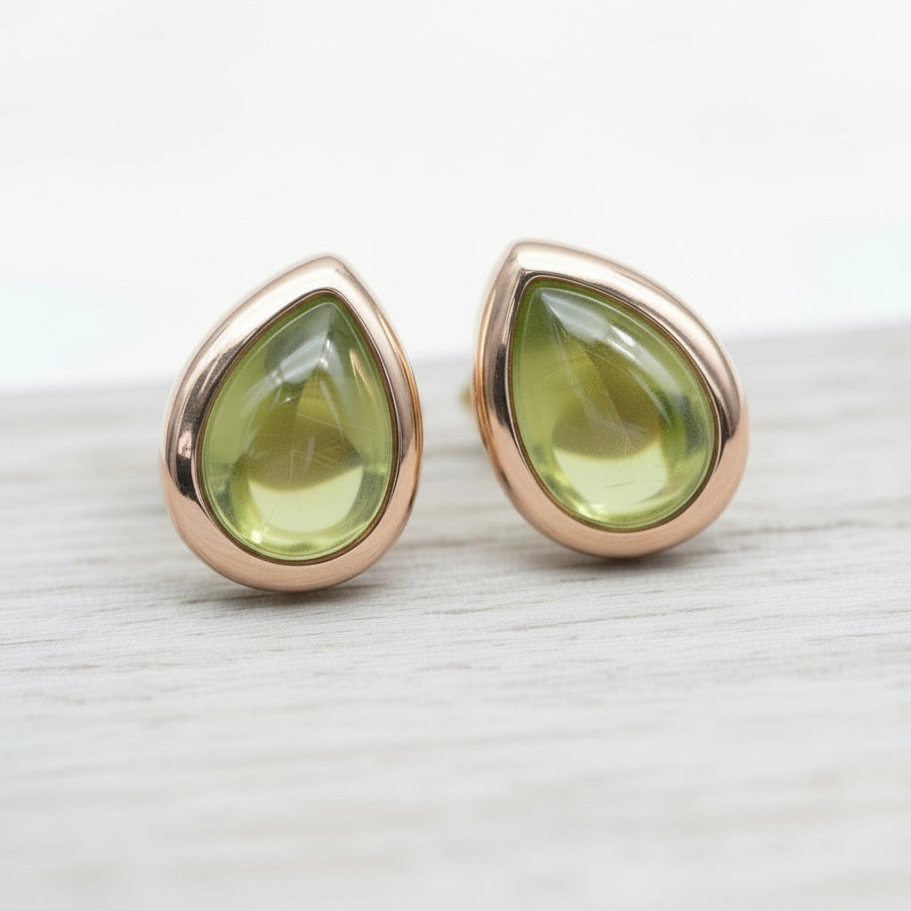 Teardrop-shaped stud earrings with rose gold frames and green peridot gemstones on a light wooden surface.