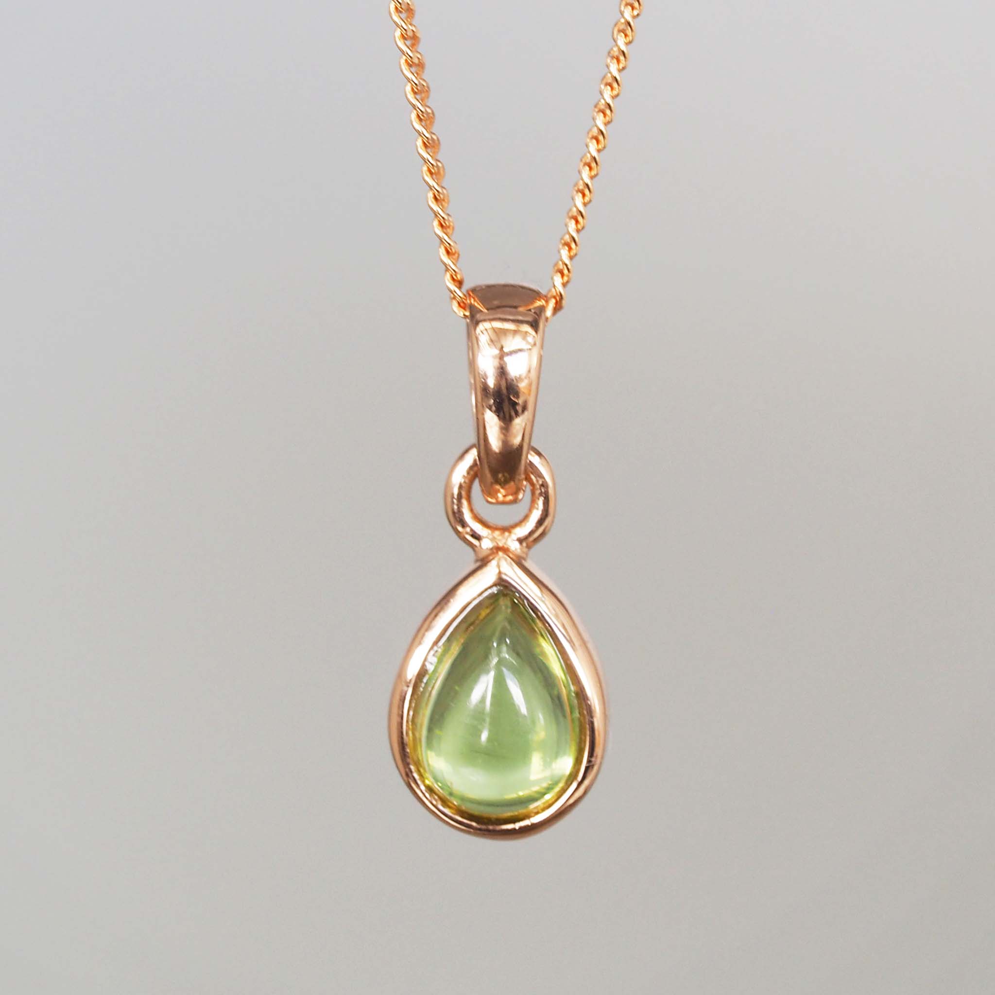 Rose Gold pendant with a green peridot gemstone on a gray background