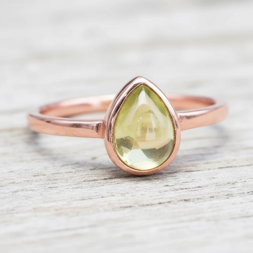 Rose gold ring with a teardrop-shaped green peridot gemstone on a wooden surface