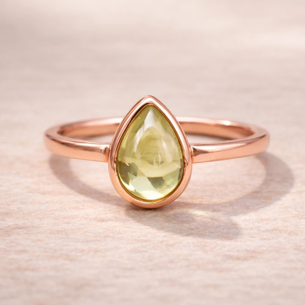 Rose gold august birthstone ring with a teardrop-shaped natural peridot gemstone on a beige background