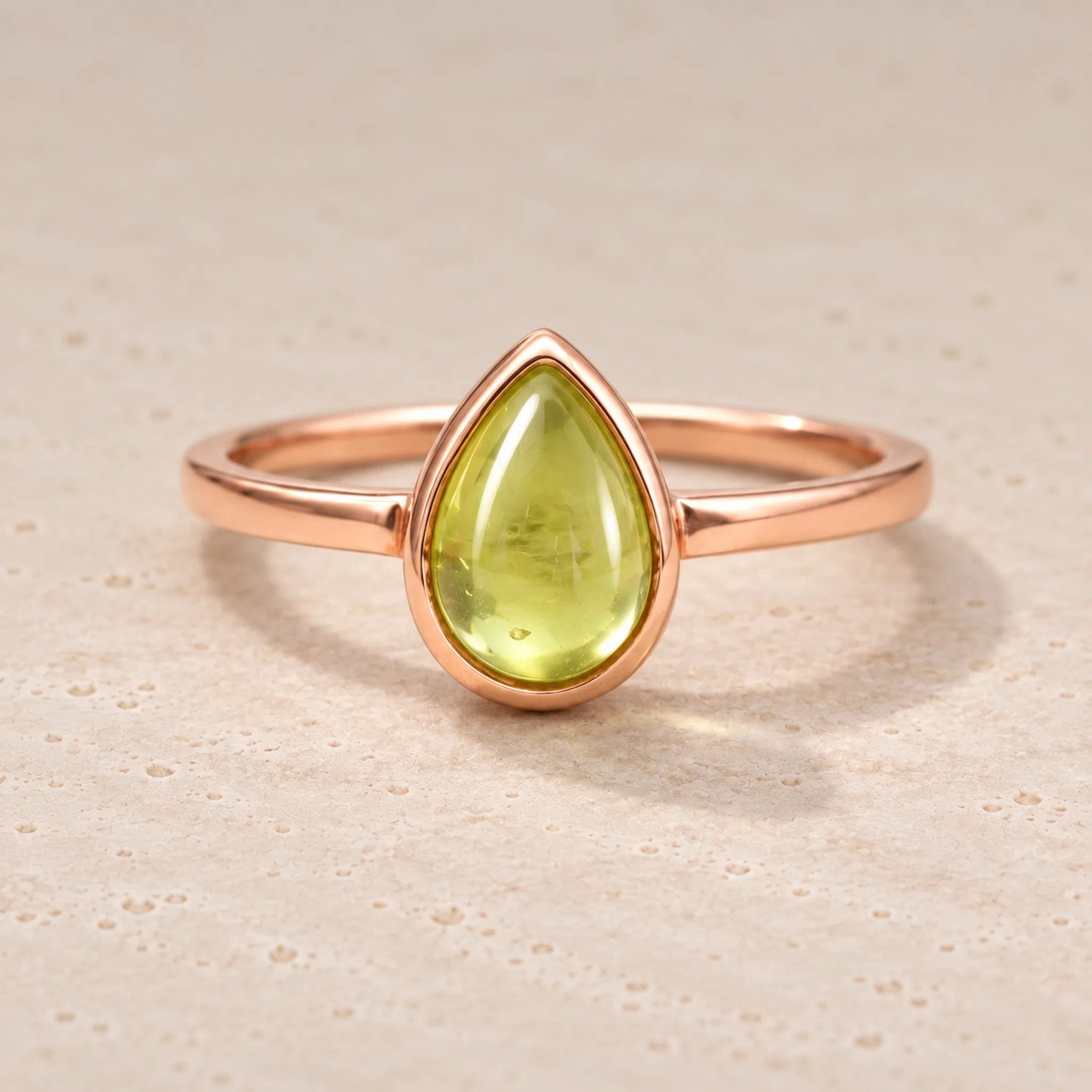 Rose gold august birthstone ring with a teardrop-shaped natural peridot gemstone on a beige background