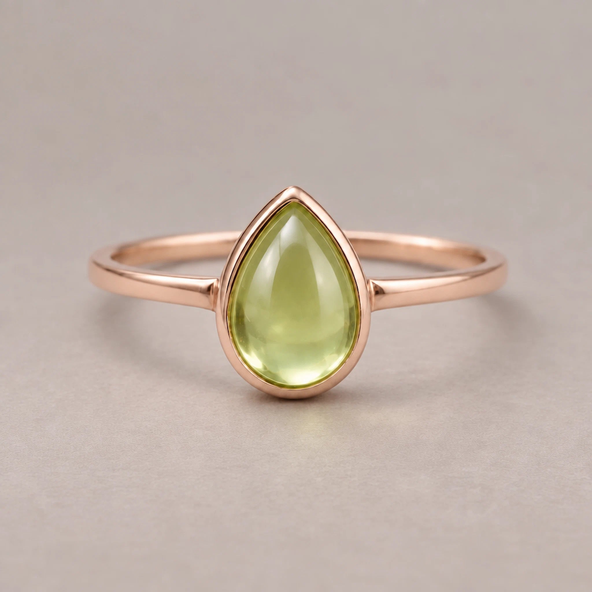 Rose gold august birthstone ring with a teardrop-shaped natural peridot gemstone on a beige background