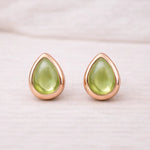 Teardrop-shaped green natural peridot gemstone stud earrings with rose gold frames on a light background