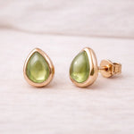Gold stud earrings with green natural peridot teardrop stones on a light background