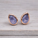 Teardrop-shaped stud earrings with tanzanite stones and rose gold frames on a wooden surface