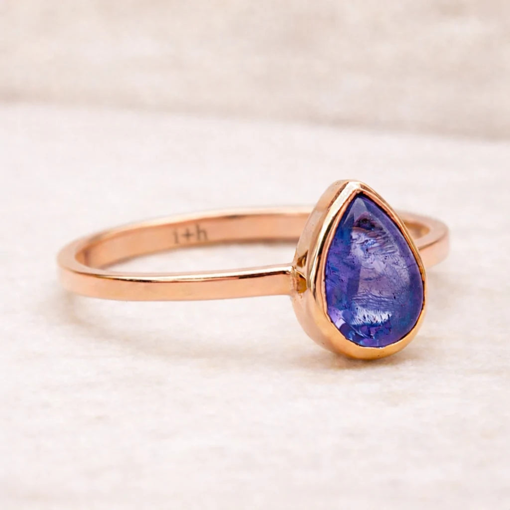 Rose gold ring with a purple teardrop-shaped natural tanzanite gemstone on a light background