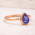 Rose gold ring with a purple teardrop-shaped natural tanzanite gemstone on a light background