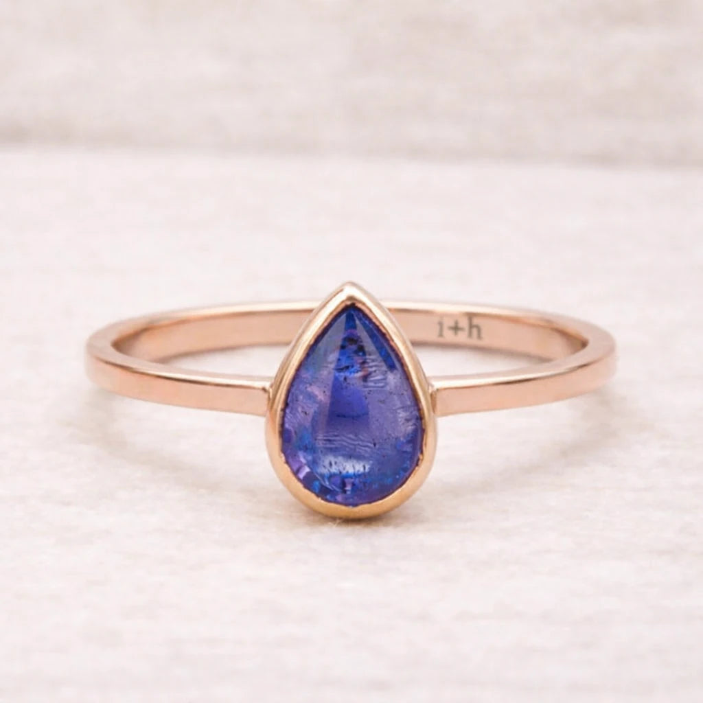 Rose gold ring with a blue teardrop-shaped natural tanzanite gemstone on a light background