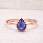 Rose gold ring with a blue teardrop-shaped natural tanzanite gemstone on a light background