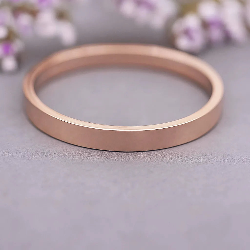 Rose gold ring on a light gray surface with blurred flowers in the background