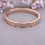 Rose gold ring on a light gray surface with blurred flowers in the background