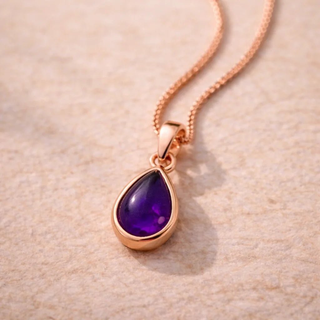 Rose gold necklace with a purple teardrop natural amethyst gemstone pendant on a beige background