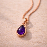 Rose gold necklace with a purple teardrop natural amethyst gemstone pendant on a beige background