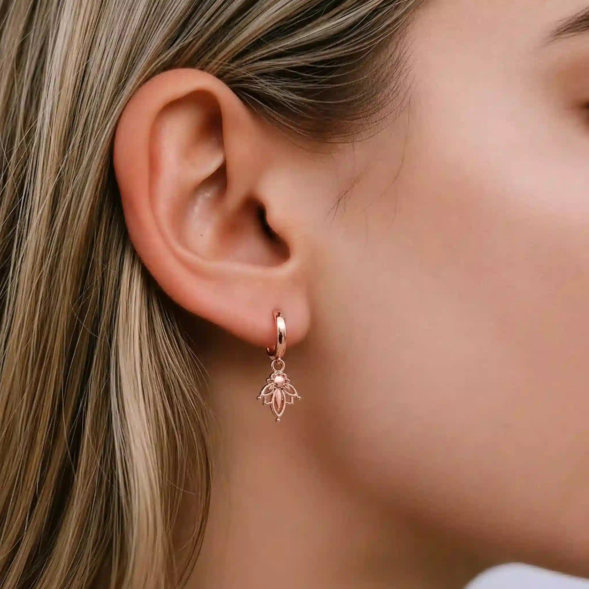 Close-up of a woman wearing a rose gold lotus hoop earring with a delicate lotus flower charm design.