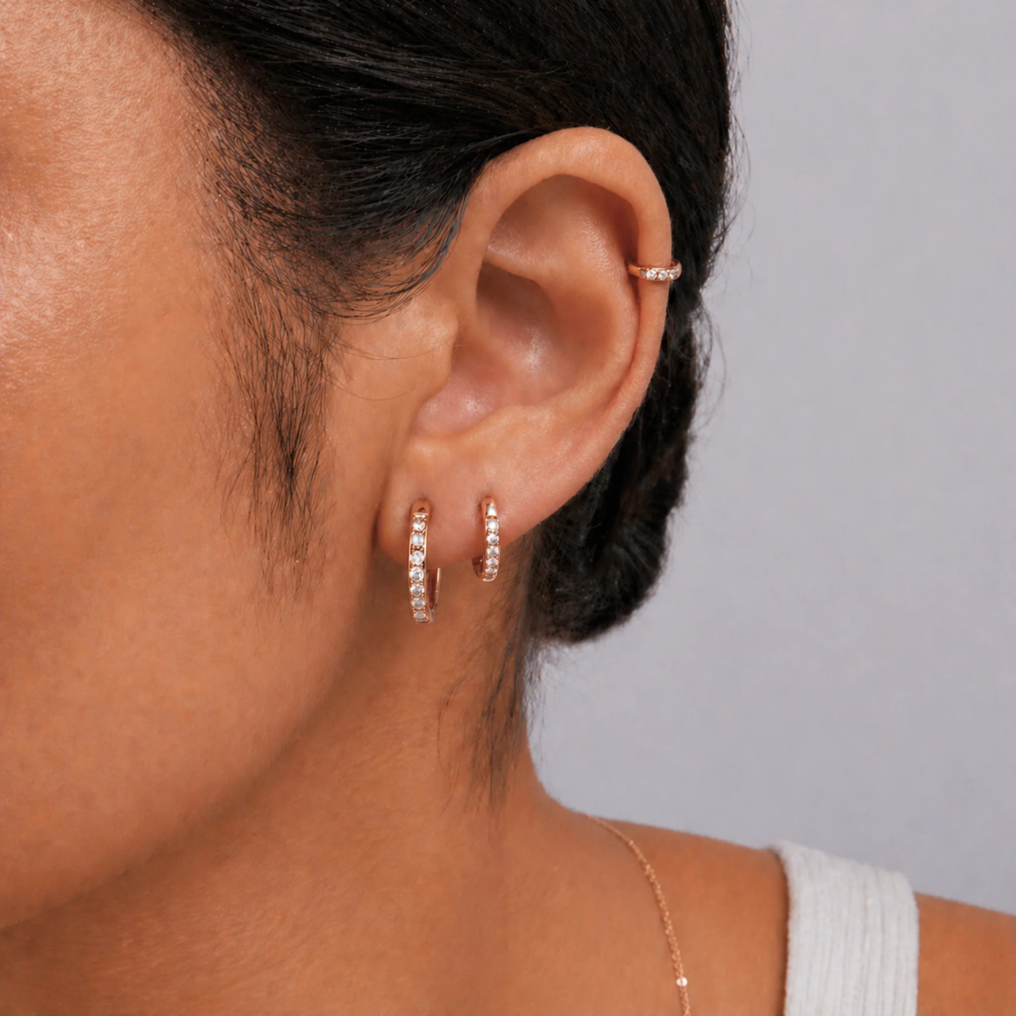 Close-up of gold waterproof pavé huggie hoop earrings worn in a stacked lobe and helix piercing arrangement