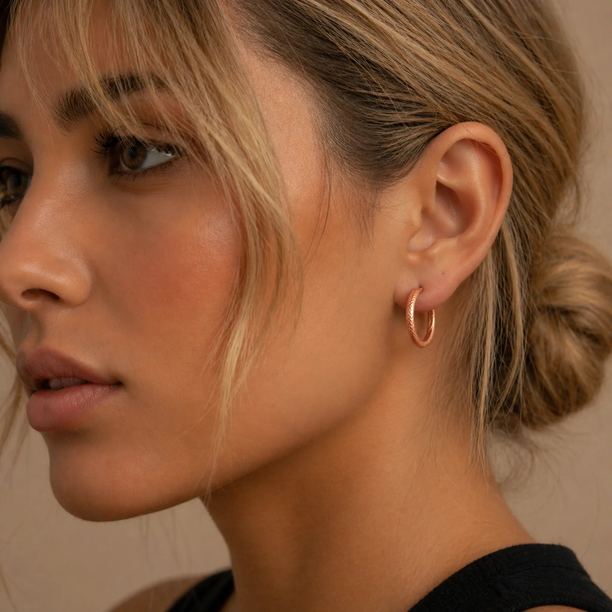 Close-up of a woman wearing a waterproof rose gold hoop earring with a neutral background