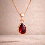 Rose gold necklace with a red teardrop natural garnet pendant on a beige background