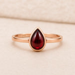 Rose Gold ring with a red teardrop-shaped january birthstone natural garnet gemstone on a beige background