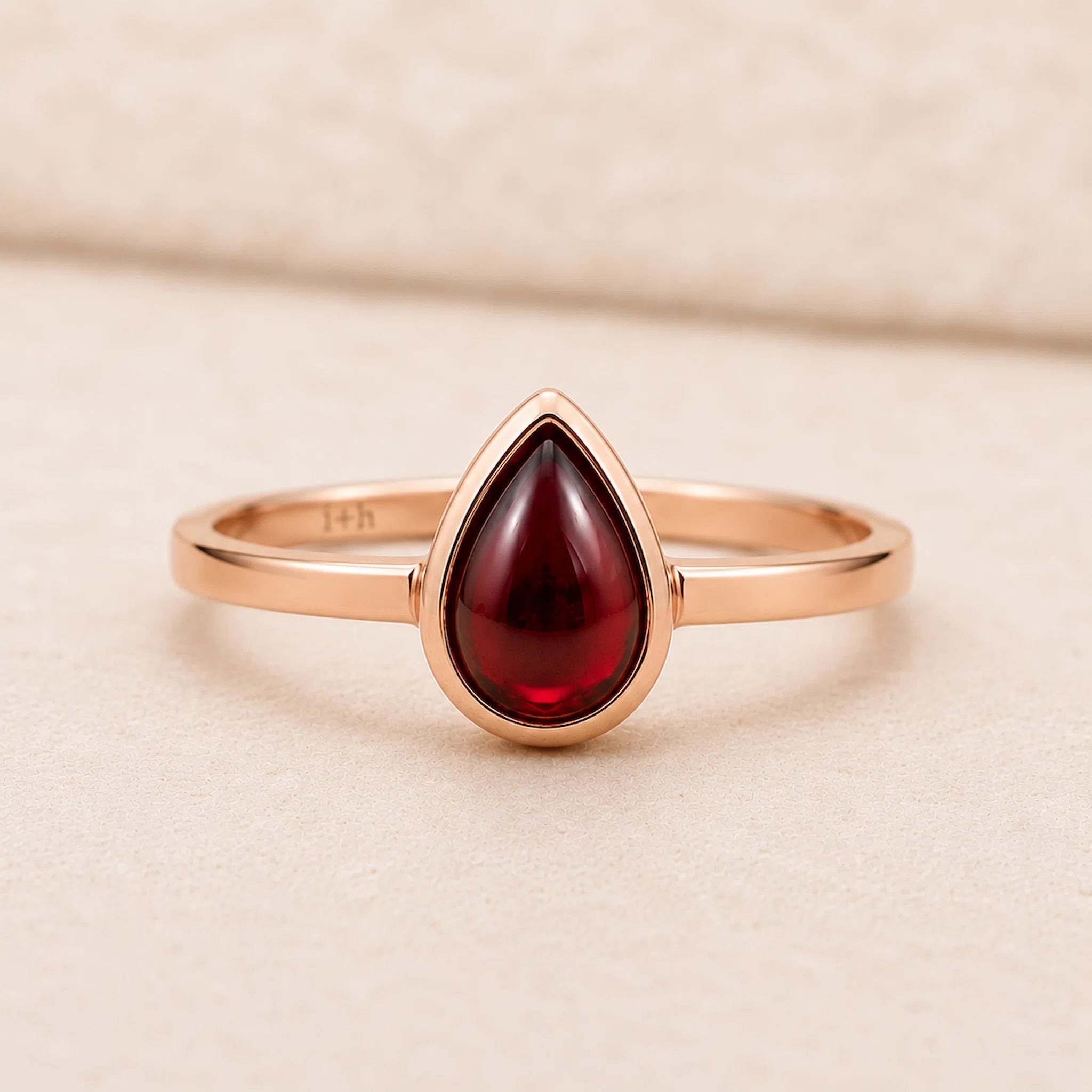 Rose Gold ring with a red teardrop-shaped january birthstone natural garnet gemstone on a beige background