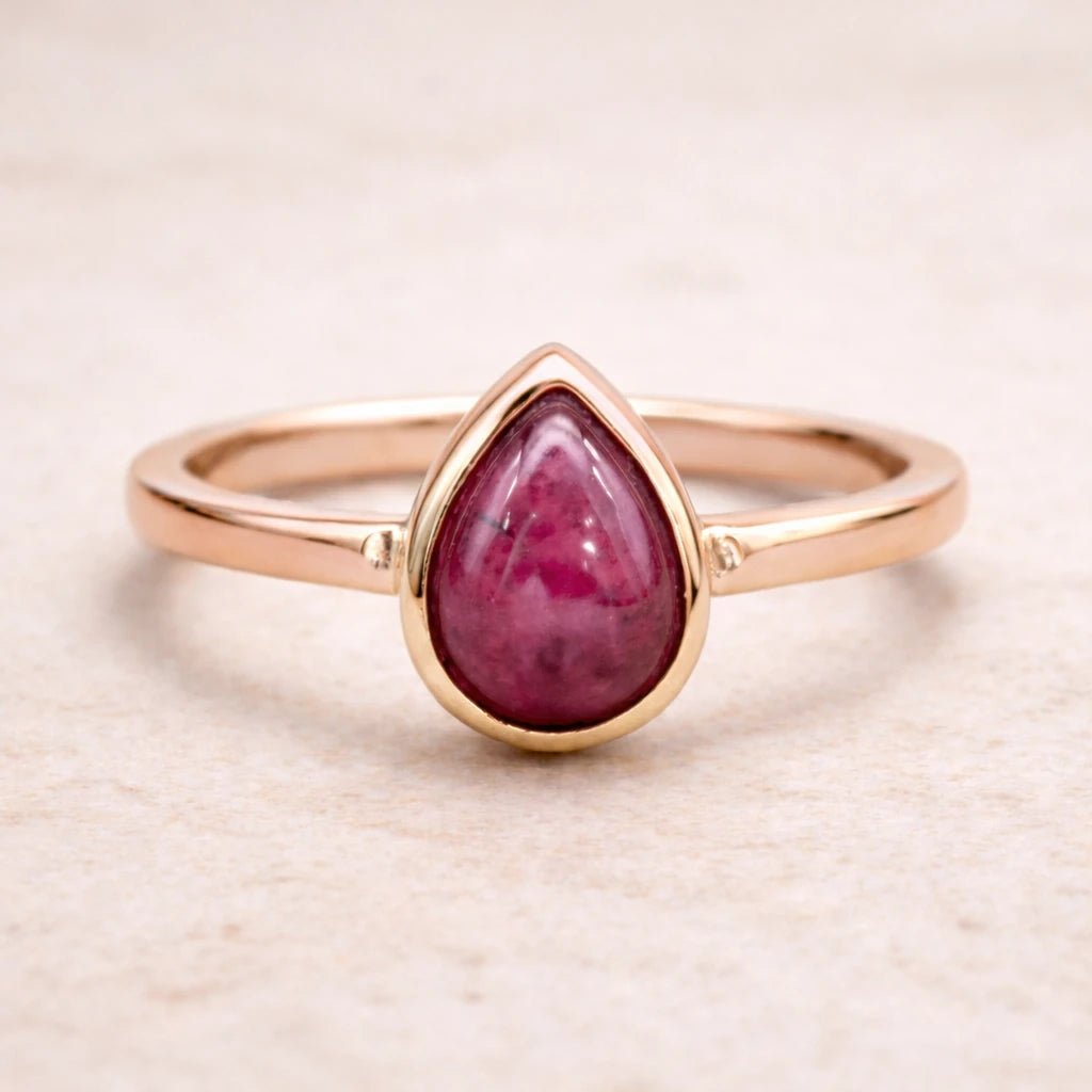 Rose gold ring with a teardrop-shaped natural ruby gemstone on a beige background
