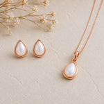Rose Gold June Birthstone Jewellery set featuring a teardrop pendant pearl necklace and matching stud pearl earrings with natural milky white teardrop pearls, arranged on a textured beige surface with dried flowers.