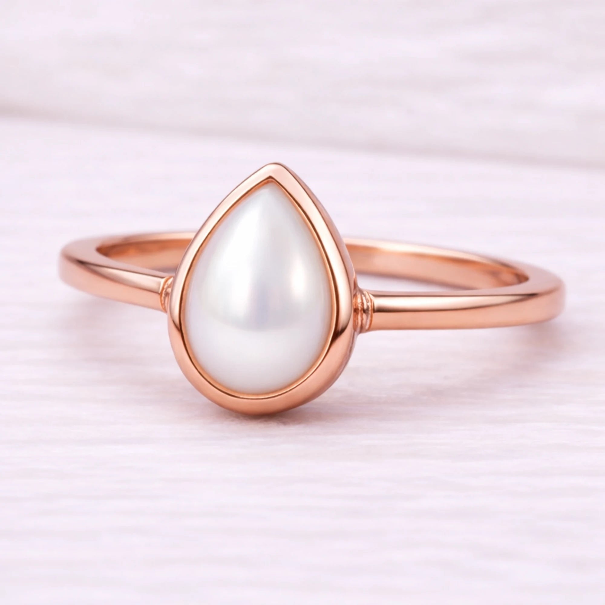 Rose gold ring with a teardrop-shaped pearl on a light pink background